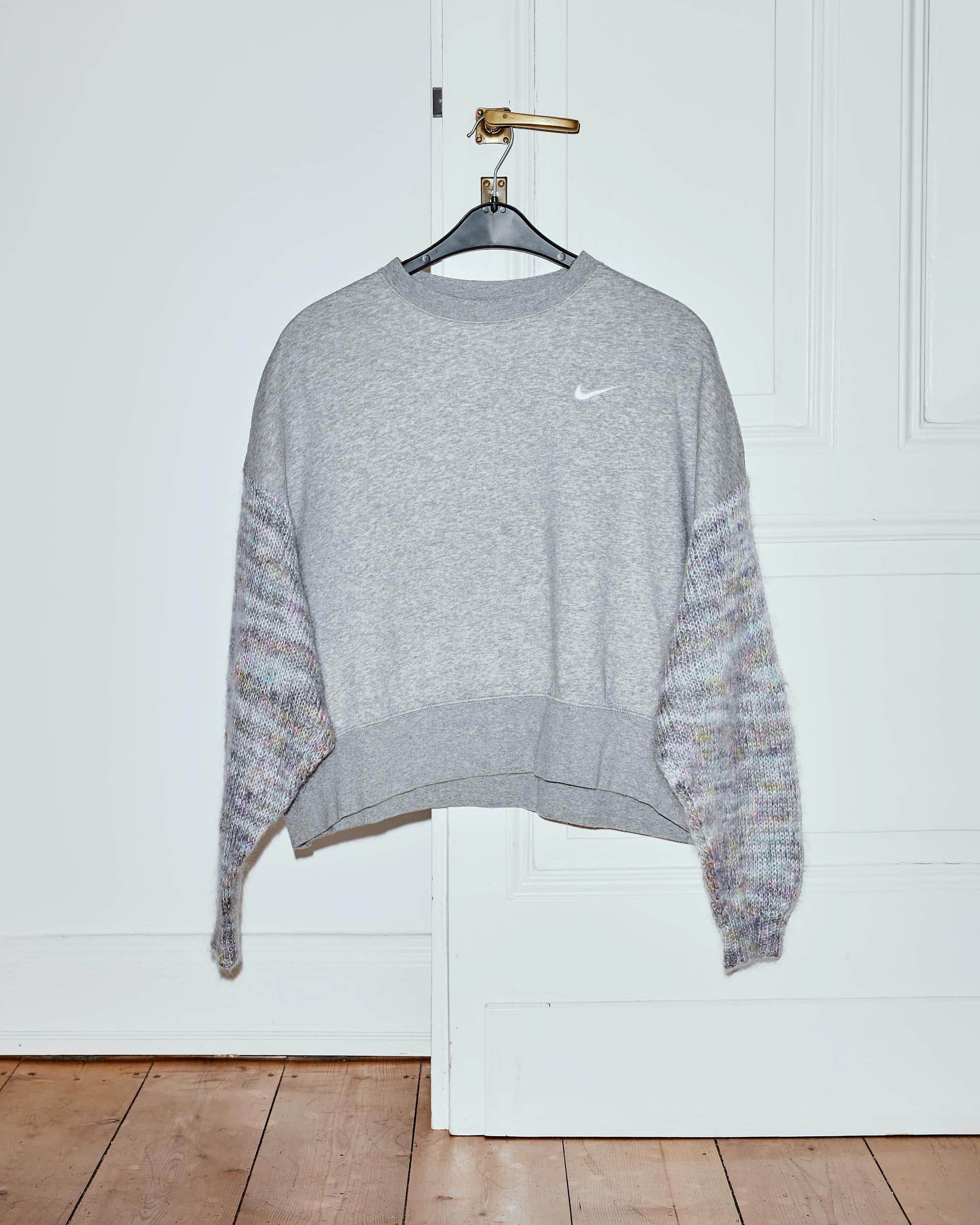 Upcycled grey Nike sweater with hand-knitted sleeves on a hanger at a door handle.