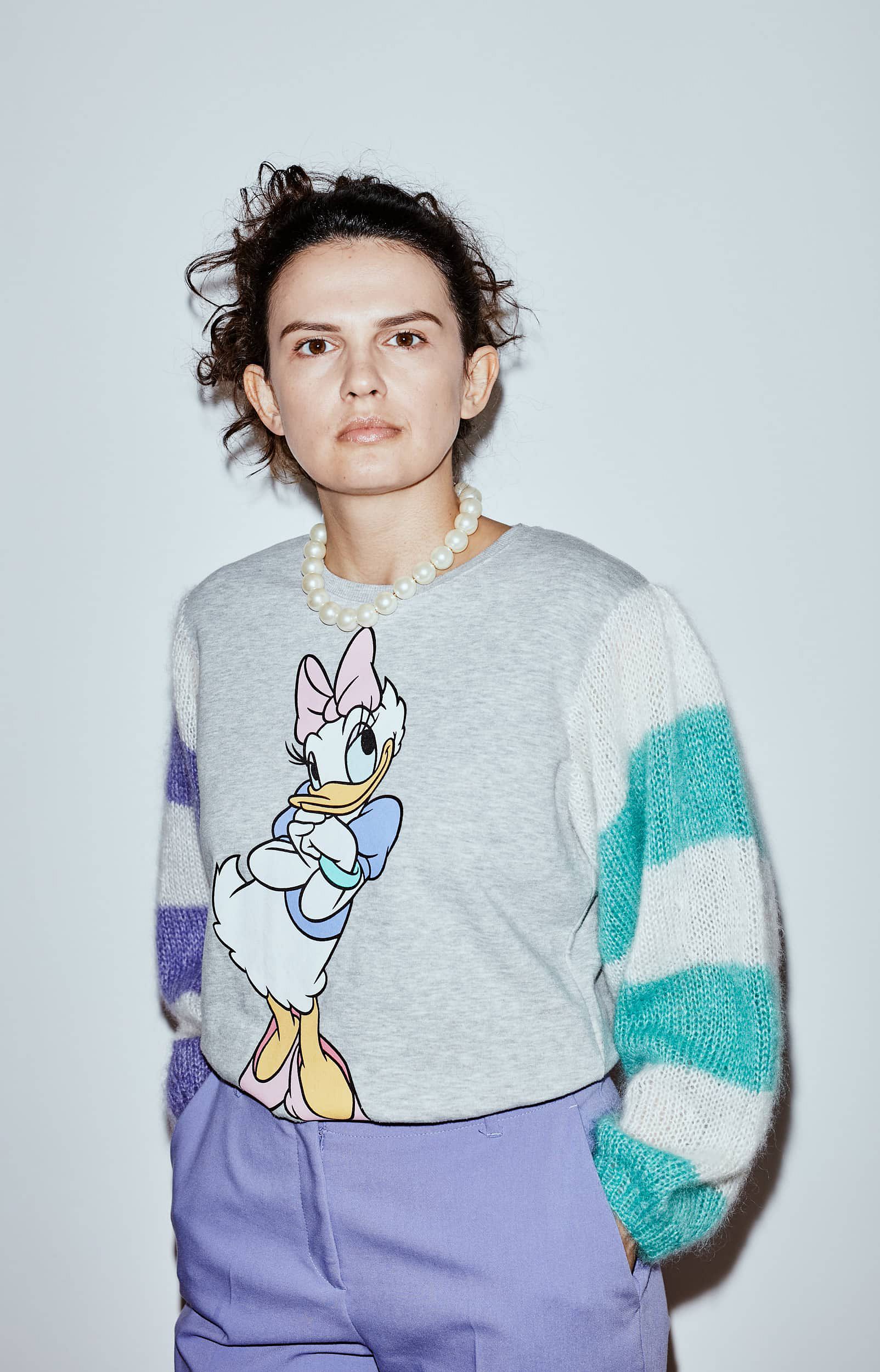 Grey second-hand sweater with Daisy Duck print and hand-knitted striped sleeves, worn by a brown-haired woman.